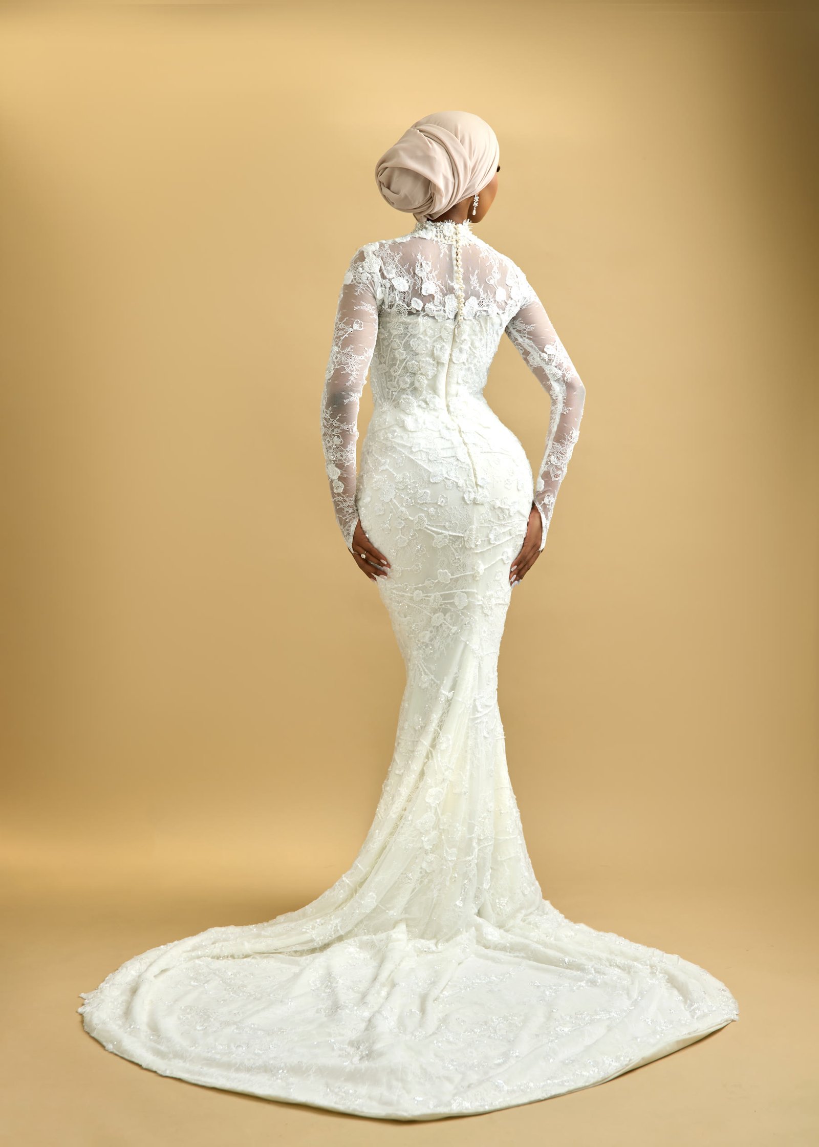 Lace bridal gown photographed from behind, showing a fuller hem and a long sweeping train