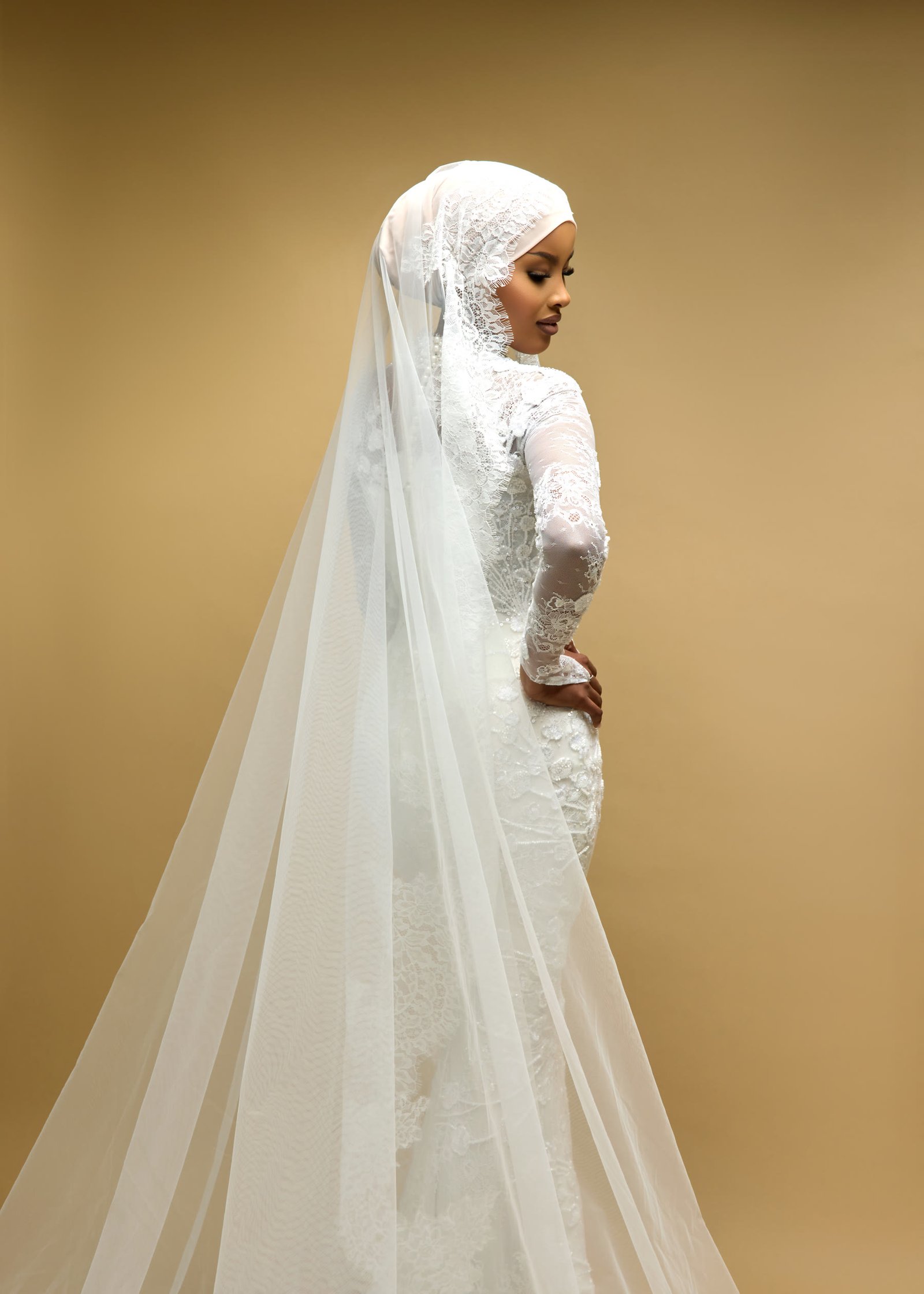 Bride in an ivory corded lace gown with long illusion sleeves, a high neckline and a cathedral veil worn over her hijab
